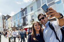 Royaume-Uni, Londres, Portobello Road, portrait d'un couple riant prenant un selfie avec smartphone